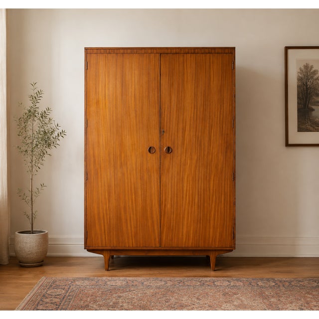 A stylish 1960s Butilux wardrobe in beautifully figured teak veneer, featuring recessed circular handles and tapered legs....