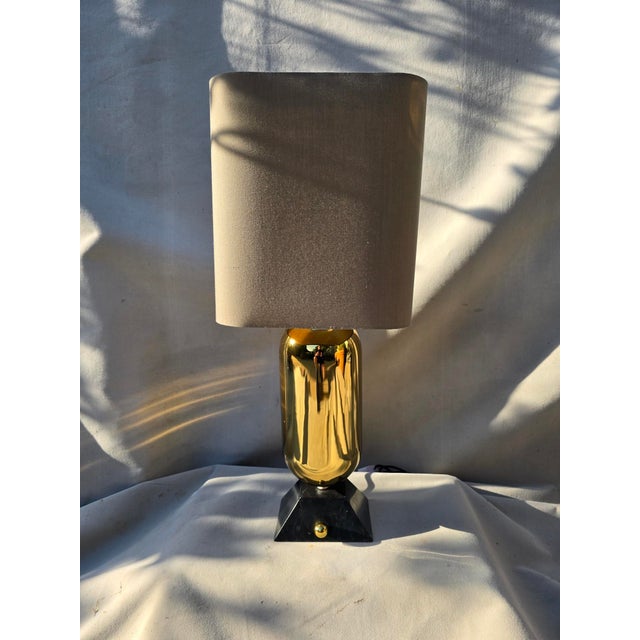 This is a unique brass lamp by Jonathan Adler. It features a polished brass capsule body and a flared black marble base....