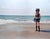 This artwork depicts a figure standing on a serene beach, wearing a helmet and gloves, which creates a striking contrast...