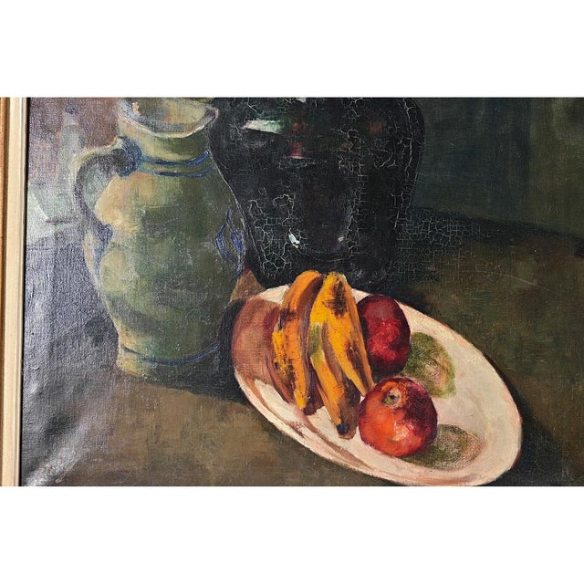This early 20th century still life is a classic composition of mixed fruits and vessels on a wood table, however the moody...