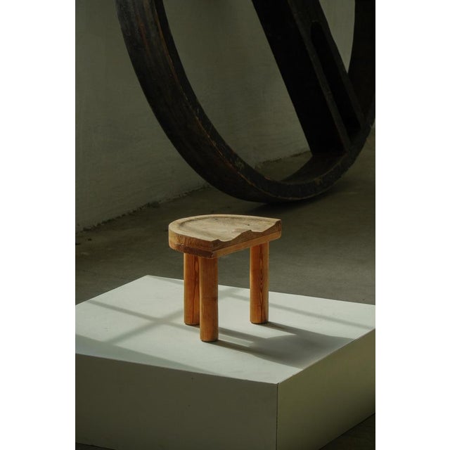 Charming Swedish folk art stool crafted from solid pine, featuring a sculptural saddle-shaped seat raised on three...