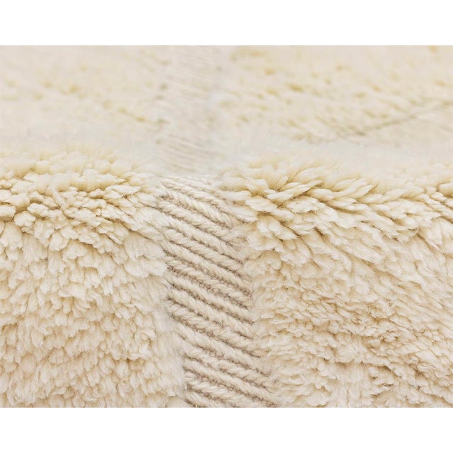 A quietly luxurious ivory rug, its plush surface carrying only the faintest hand-woven diamond pattern — a study in...