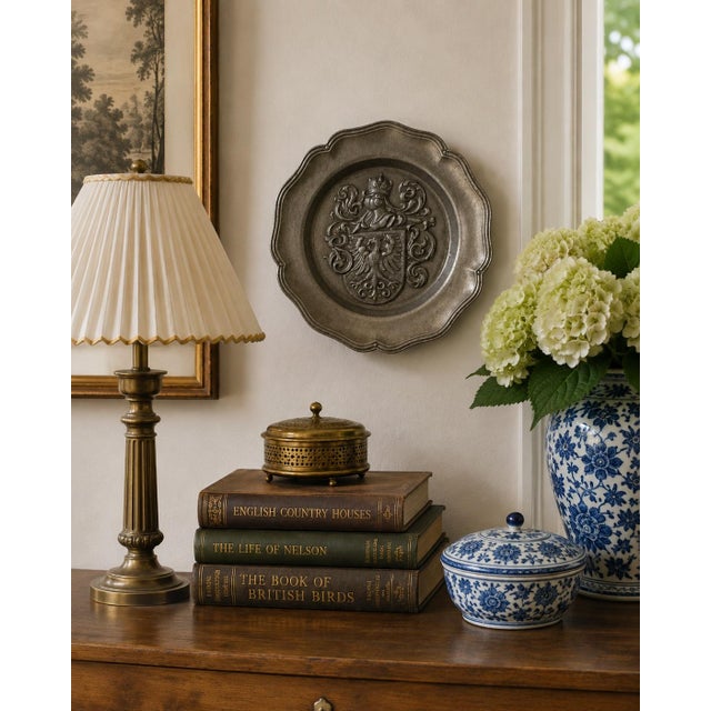 A handsome mid-20th-century German pewter wall plate centered by a richly modeled heraldic coat of arms. The shield bears...