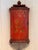 A hanging corner cupboard with a bowed front, painted overall on a red ground with gilt scrollwork cartouches enclosing...