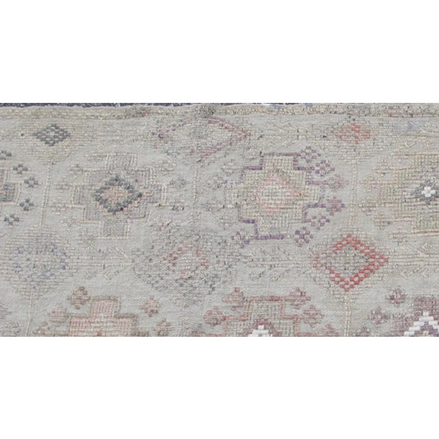 Measures 4'7 x 8'0 This rug features an asymmetrical design of tribal crests decorating the light blue-grey field. The...