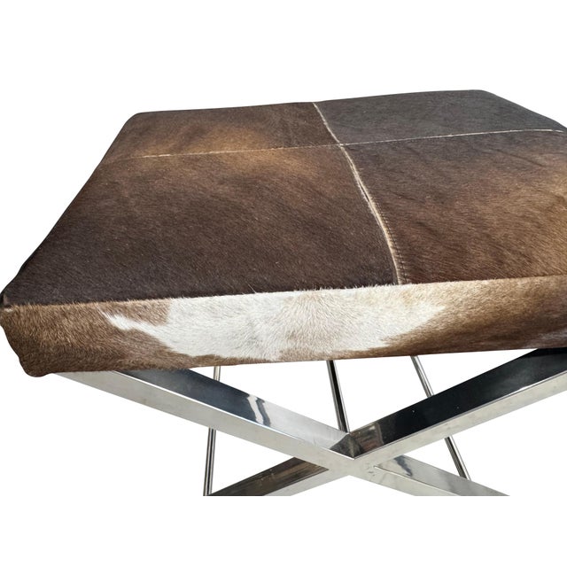 Pair of mid-century cowhide-covered benches with chrome cross bases. Natural cowhide in brown and white with tan...