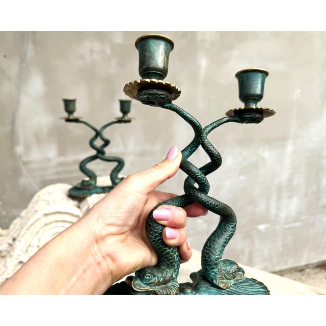 A sculptural pair of Italian cast bronze candlesticks featuring elegantly intertwined fish rising from shell-form bases....