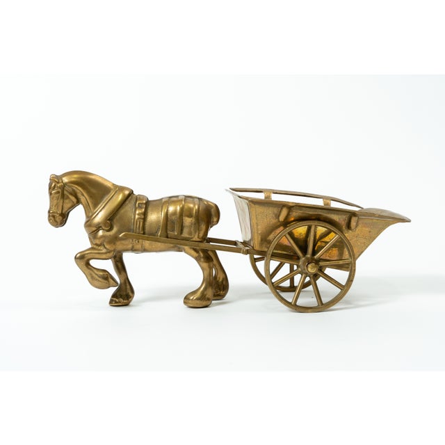 The object is an elegant, hand-cast brass horse figurine, behind which is a stylized, two-wheeled horse-drawn carriage....