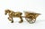 The object is an elegant, hand-cast brass horse figurine, behind which is a stylized, two-wheeled horse-drawn carriage....