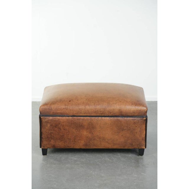 Characterful sheepskin footstool/ottoman with a beautiful patina and finished with black piping. This characterful...