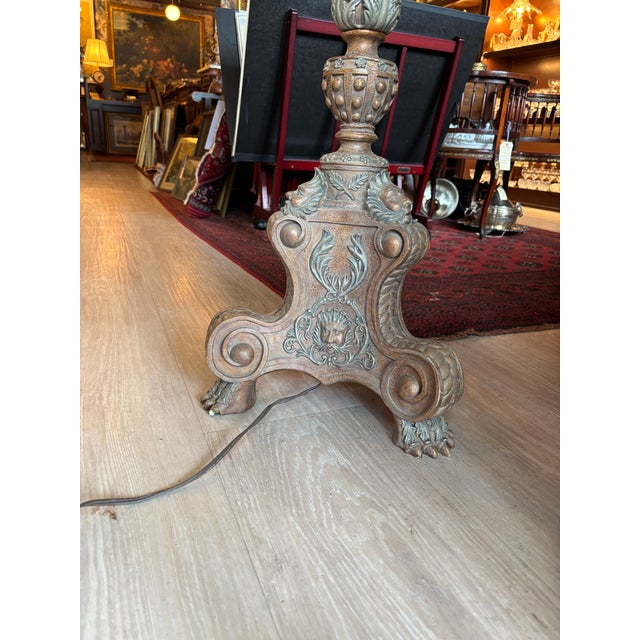 A striking antique carved wood torchiere floor lamp featuring elegant claw feet, a beautifully detailed Roman head motif,...