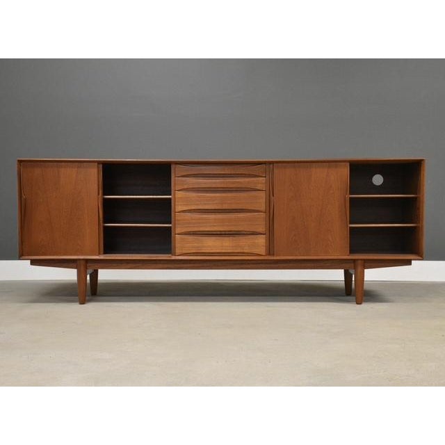 A mid century modern teak credenza with four sliding doors, five drawers, and sculpted pulls designed by Arne Vodder for...