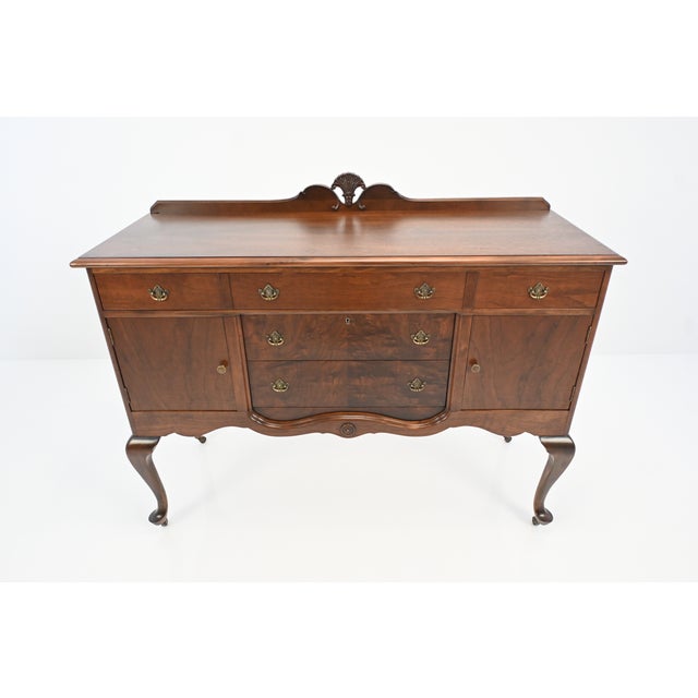 An elegant American Queen Anne Revival walnut sideboard by Baker Furniture, circa 1920s, featuring a gracefully serpentine...