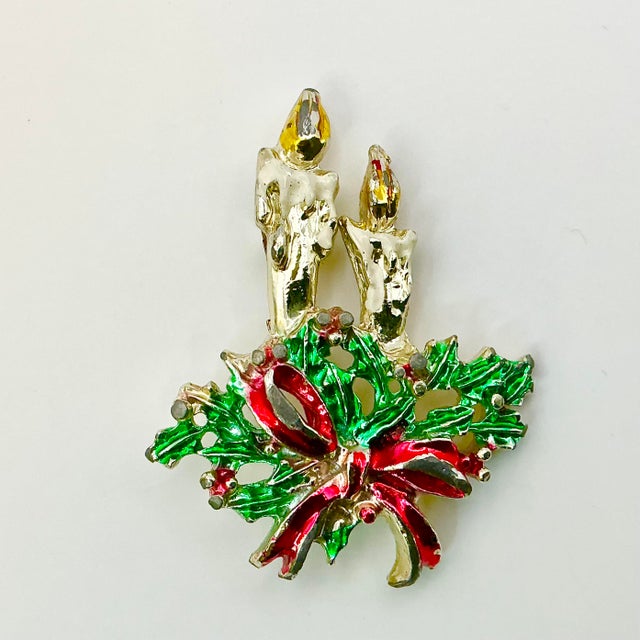 A lovely Christmas Brooch from the 1960s. It features two lit candlesticks nestled in green holly with red berries and red...