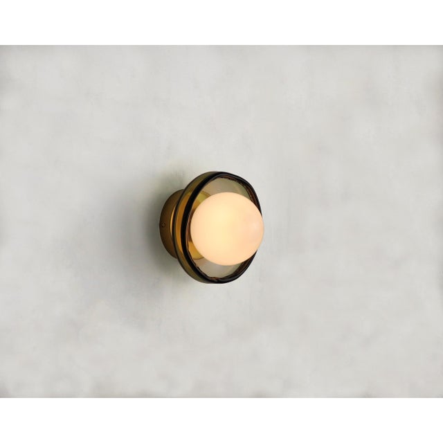 This small wall light is crafted from hand-blown glass, offering a delicate yet expressive presence. Its compact scale...
