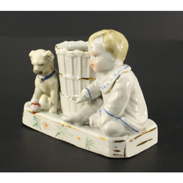 A lovely fairing porcelain figural match holder It features a baby and a puppy, both very cute, seating next to a large...