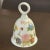 Lovely white porcelain bell with a different floral & butterfly motif on each side. Silver trim along the top near the...