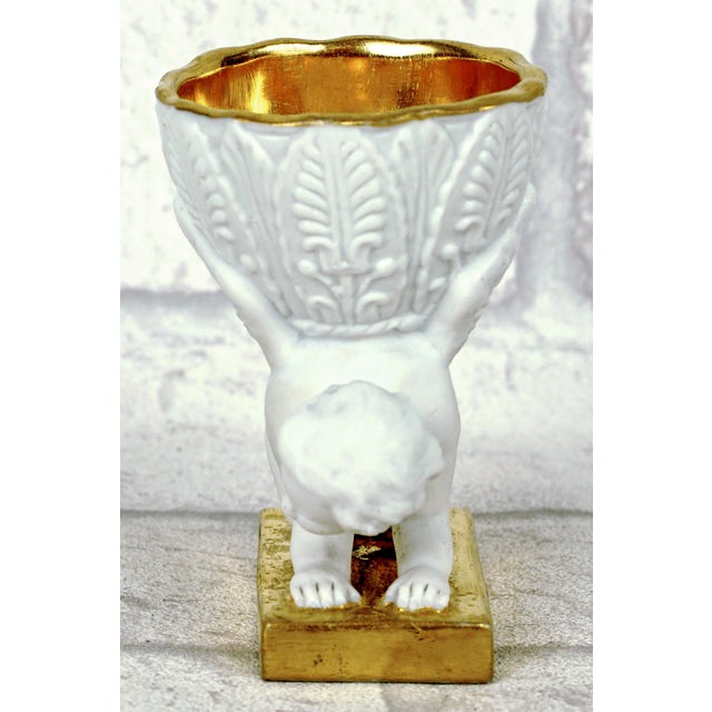 Of sculptural and figurative form, resting on a quadrangular base entirely decorated in gold, the stem is formed as a...