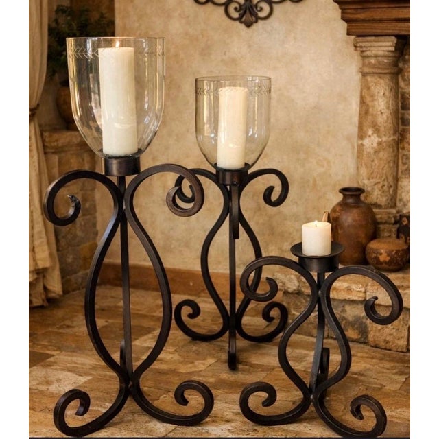 Striking set of three oversized iron floor candelabras featuring dramatic hand-forged-style scrollwork and substantial,...