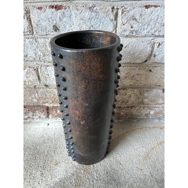 Tall vintage ceramic vase, featuring a dark bronze finish and distinct raised studs running vertically down the body of...