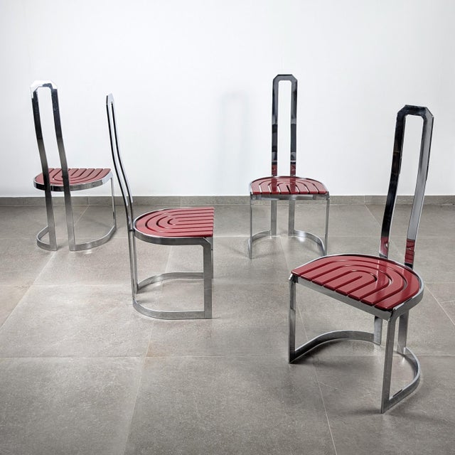 Set of four dining chairs with a flat-profile chromed steel frame and red lacquered wooden seats. The design emphasizes...