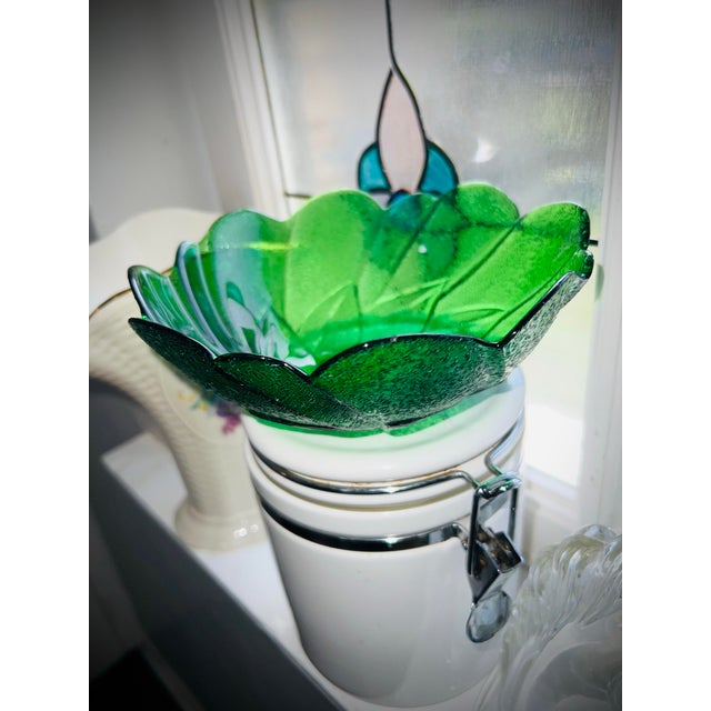 A vintage green pressed glass bowl with a scalloped edge and raised leaf motif. The glass has a textured, pebbled surface...