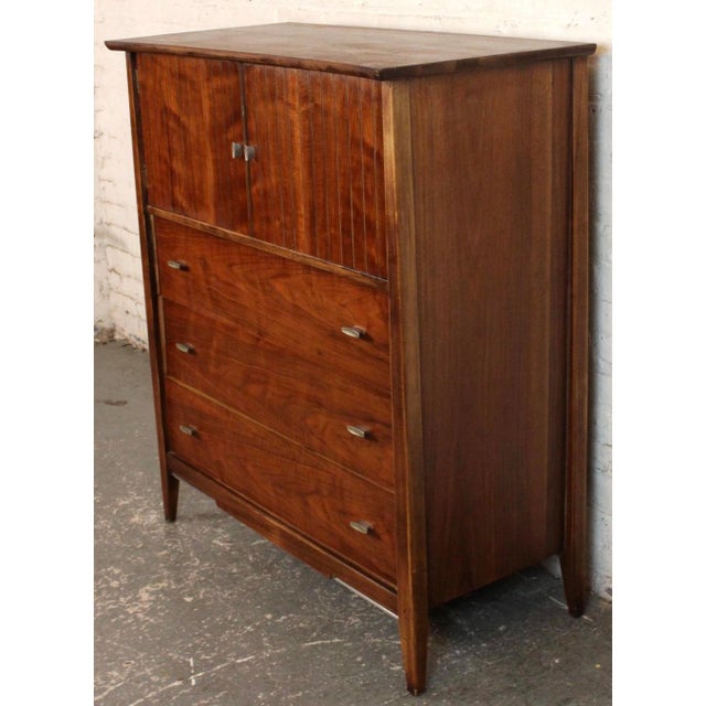 This elegant Mid-Century walnut highboy dresser by Harmony House features clean lines, sculpted drawer pulls, and a rich...