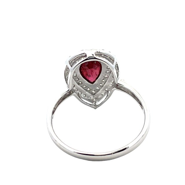 18K gold ring featuring a 0.88-carat pear-cut red ruby, surrounded by 0.29 carats of round-cut white diamonds. The design...
