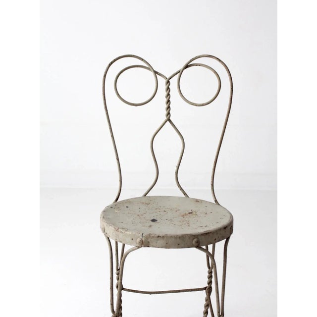 A vintage ice cream parlor chair crafted in painted Gainsboro light gray metal, featuring an ornate silhouette with...