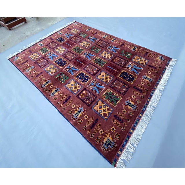 This hand‑knotted Afghan wool rug is inspired by traditional Turkoman‑derived tribal designs and features a rich rust...