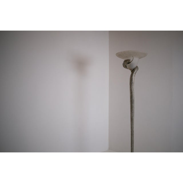 A silvered bronze floor lamp depicting a serpent rising from its base to embrace a frosted glass shade. This light fixture...