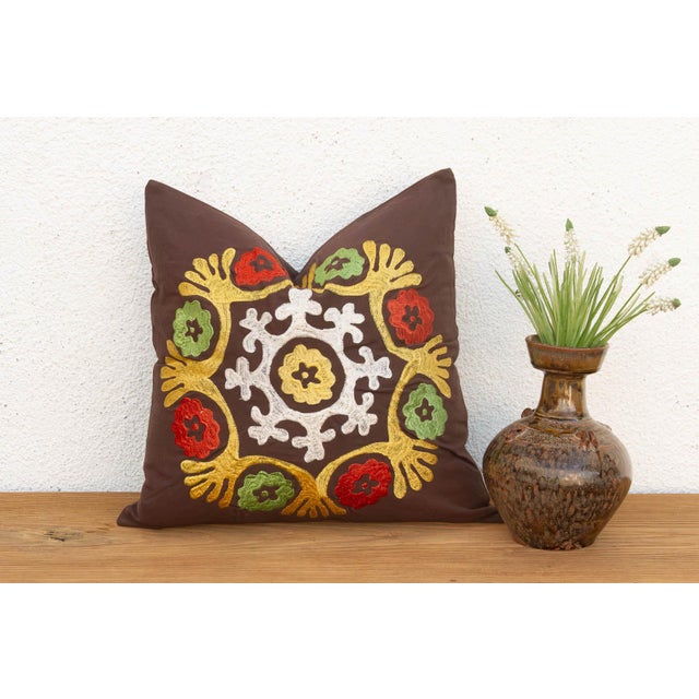 A radiating medallion in mustard-gold, worked as stylized wing-like forms reaching outward, frames a cluster of red flower...