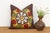 A radiating medallion in mustard-gold, worked as stylized wing-like forms reaching outward, frames a cluster of red flower...
