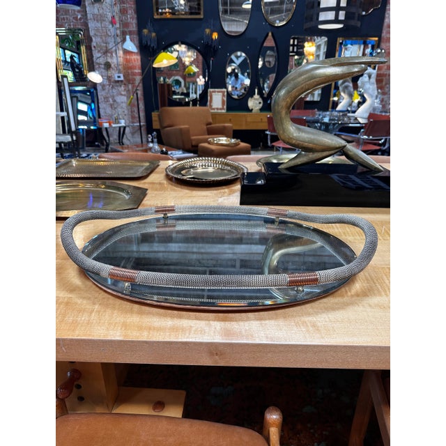 The "Vintage Italian Decorative Tray, 1960s" features a mirror base and a stylish chrome handle encircling the base. This...