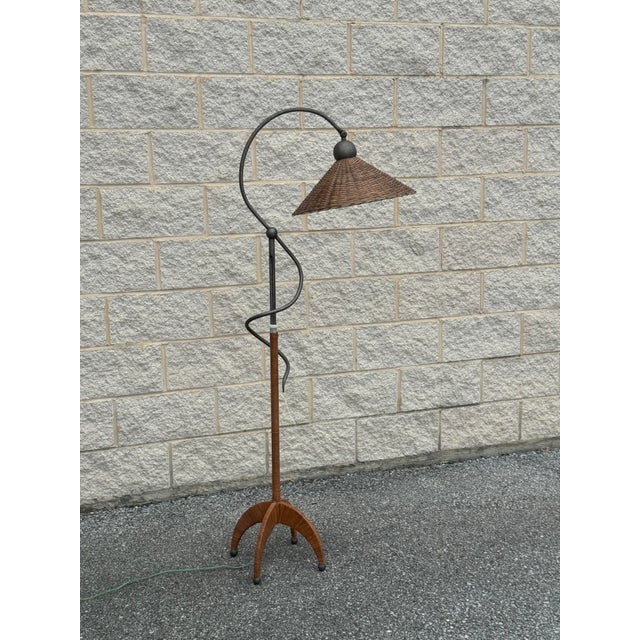 An elegant vintage floor lamp combining a sculptural black metal frame with natural woven wicker elements.
