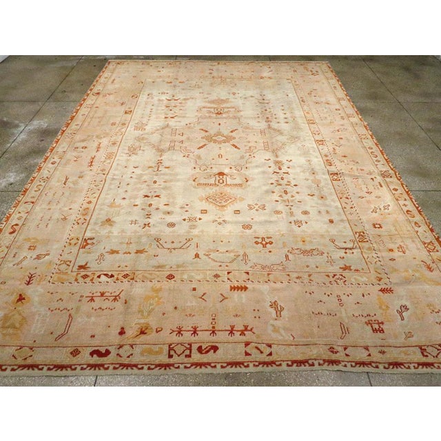 An antique Turkish Oushak room size carpet. The ivory field centers a beige four armed medallion with stylized pendants...