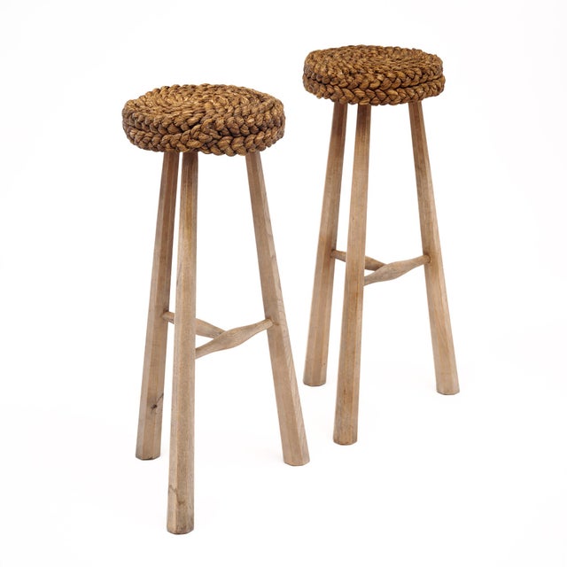 Pair of French stools by Audoux Minet. Each stool is made with a braided wicker seat on a hand carved tripod wooden...