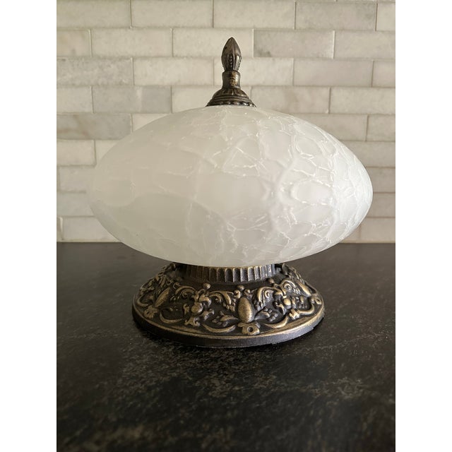 This flush mount ceiling light from the mid-1970s has a large ornate cast metal fitter embossed with scrolls and leaves...
