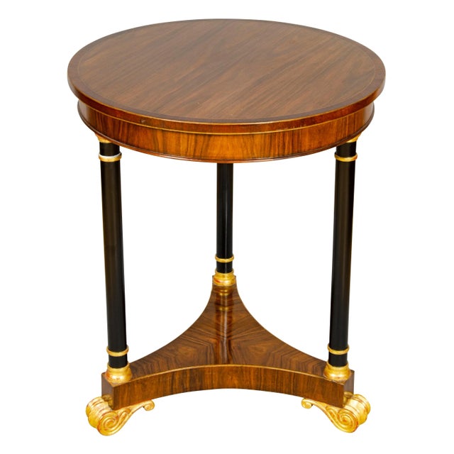 Circular banded top over a conforming frieze supported on three ebonized and gilt wood legs joined by a plinth base raised...