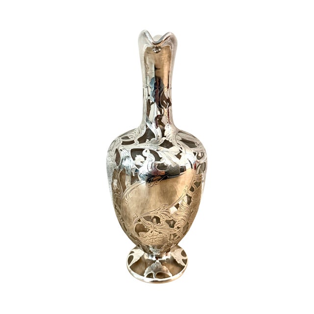 A graceful glass pitcher elevated by sterling silver overlay in a grapevine motif, dating to circa 1900. The silhouette —...