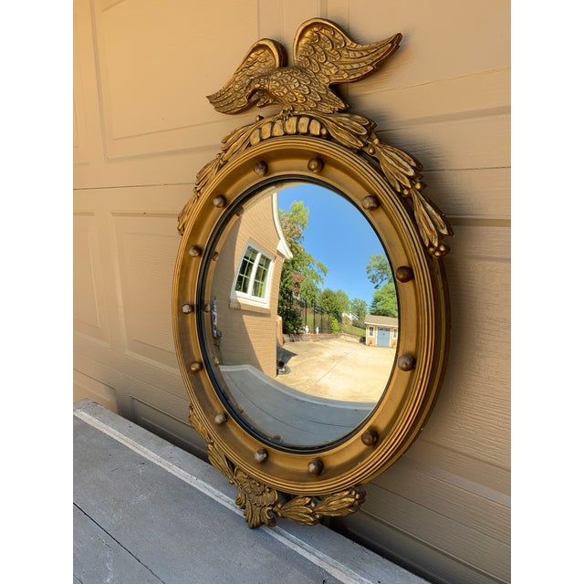 A gorgeous Federal or Regency style convex bullseye wall mirror featuring a carved eagle with open wings standing on olive...