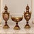 Elegant three-piece French-style porcelain garniture set featuring two matching covered vases and a coordinating central...