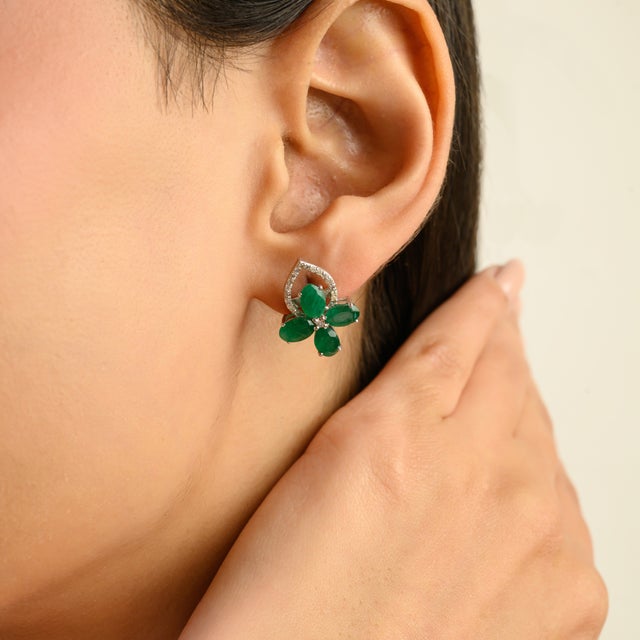 Graceful silver earrings featuring a lush emerald floral cluster paired with an elegant open heart silhouette accented in...