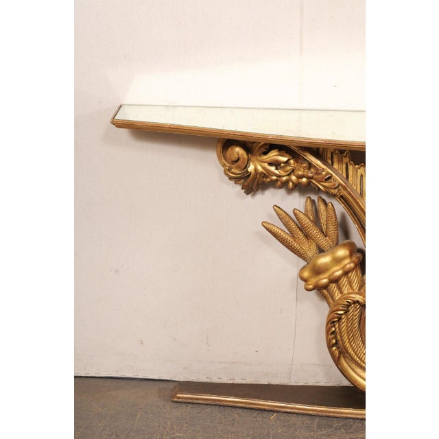 An Italian cornucopia motif carved and gilt wood wall console with mirrored top from the early 20th century. This antique...