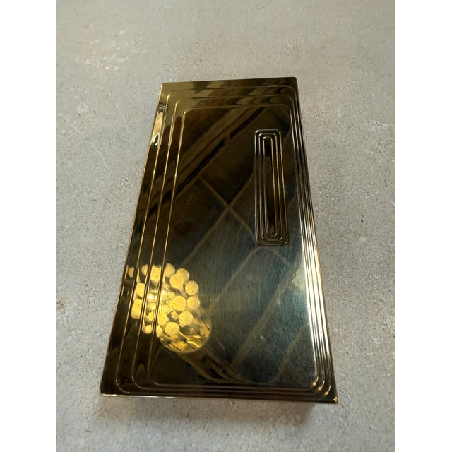 Sleek vintage brass box featuring a clean rectangular form with subtle geometric detailing on the lid. The stepped, linear...