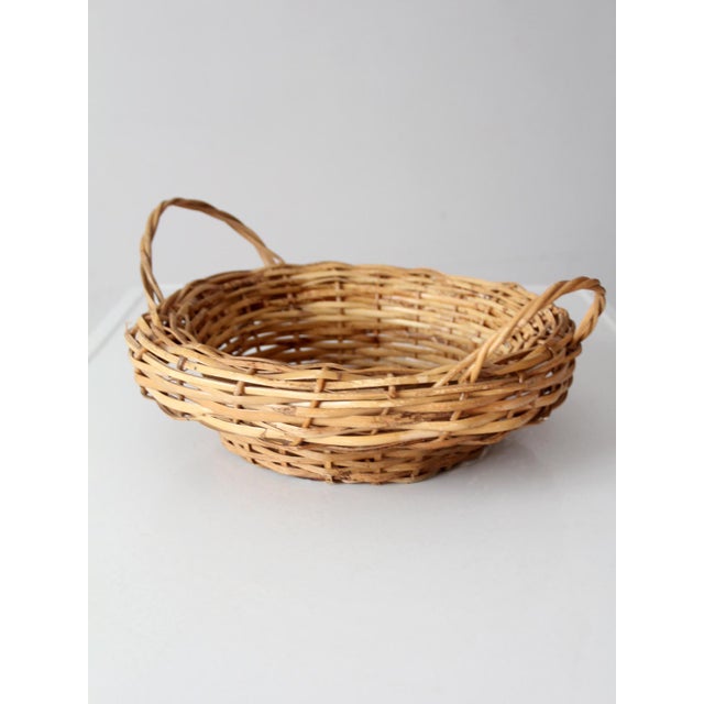 A vintage round wicker basket with a broad woven rim, raised base, and two loop handles. Beautifully varied natural wicker...