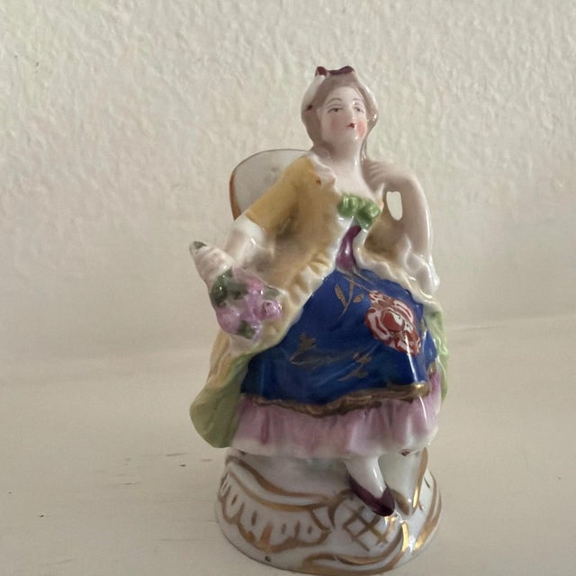 Thes two small figurines depict a seated man and woman wearing clothing typical of 18th century European courtiers.