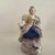 Thes two small figurines depict a seated man and woman wearing clothing typical of 18th century European courtiers.