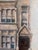 A charming vintage oil painting depicting a tall Victorian-era townhouse with projecting bay windows, architectural...