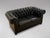 A good quality mid 20th-century two seater black leather chesterfield with two loose cushions, raised on ebonised bun...